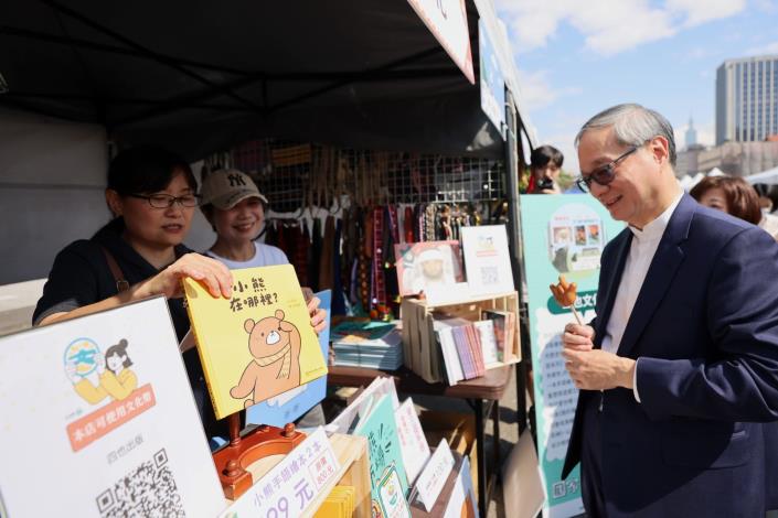 「國家語言生活節」現場有超過50攤的創新書市，展出母語學習、母語文化及文創商品等，還有手語繪本吸引文化部長李遠（右）駐足暸解。
