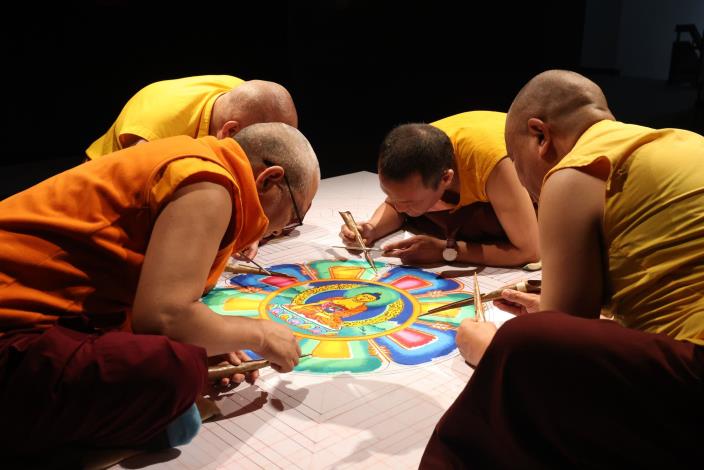 Four lamas are painting a mandala