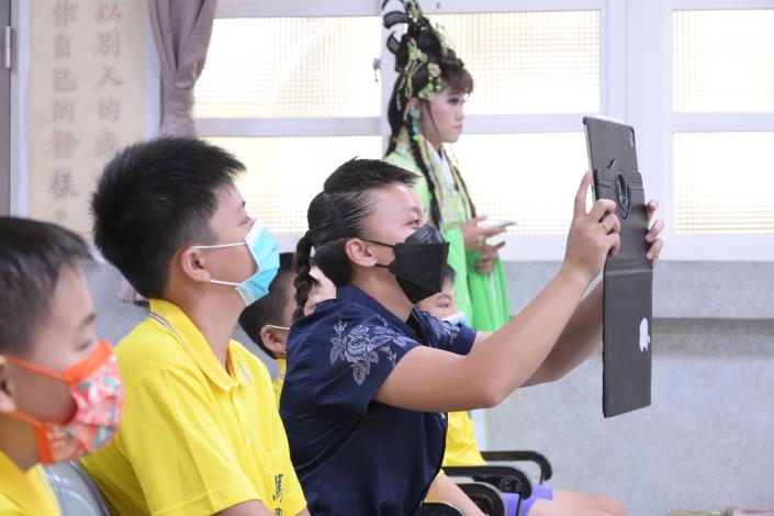 江怡璇（右坐者）在疫情期間仍做好防護，前進校園，導入AR與歌仔戲互動式學習。