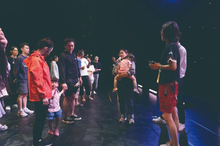 劇團就像個大家庭，大人緊鑼密鼓排練時，孩子就在旁邊玩耍。孩子玩累睡著了，漪珮一手抱著孩子，一手拿著麥克風，把握時間和大家開會，上演職業婦女的日常。（榮興客家採茶劇團提供）