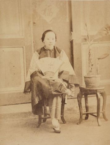 〈婦人〉 日人廣部正三於1896年2月至臺灣遊歷，〈婦人〉為其收集、製作之臺灣影像寫真帖內照片之一。 本照片為在室內攝影的一婦人，旁邊有盆栽。婦人頭髮往後梳，微露齒而笑，眼神自然。穿著大襟衫，右手持扇，左手腕戴著玉環。婦人纏足，但蹺腳拍照，姿態怡然自得。