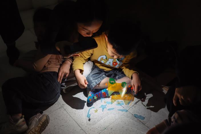 13光與影的紅綠燈派對：孩子拿著完成的車子戲偶，在光影情境中模擬交通情境。