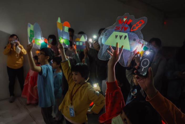 12光與影的紅綠燈派對：孩子拿著完成的車子戲偶，在光影情境中模擬交通情境。