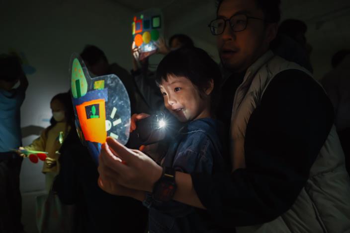 11光與影的紅綠燈派對：孩子拿著完成的車子戲偶，在光影情境中模擬交通情境。
