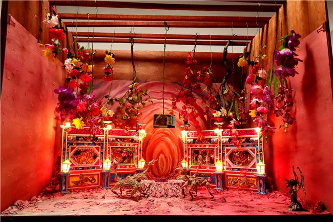 張徐展作品〈紙人展–房間〉，暗紅色的祭壇中蜷曲著一隻紙偶-小黃，走獸們圍繞著跳舞，是慶祝還是哀悼，一如生命的糾結與怪誕的情緒。