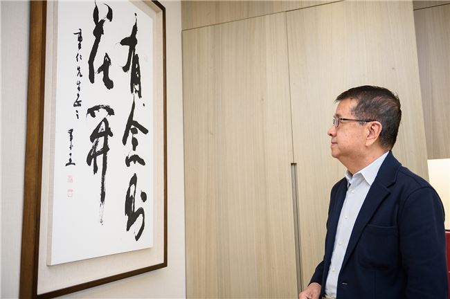 徐重仁辦公桌旁掛著一幅字畫，「有念者花開」五個大字是他數十年的信念。